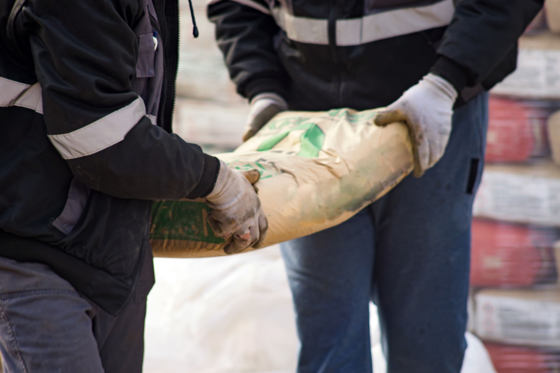 Two construction workers carry a bag of cement midsection close up at the warehouse